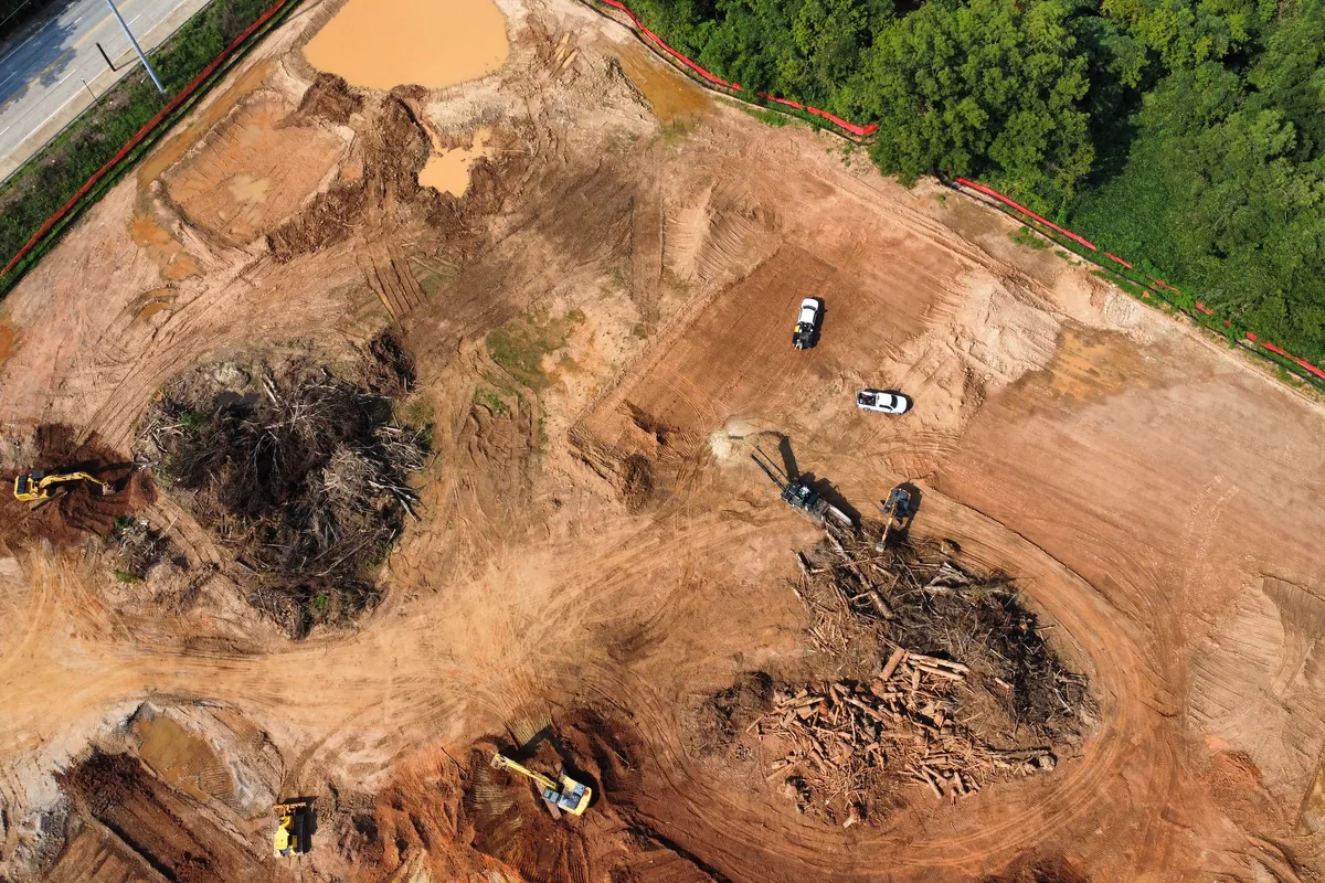 Overhead view of a large Georgia clearing site with excavators, a dozer, and brush piles being worked